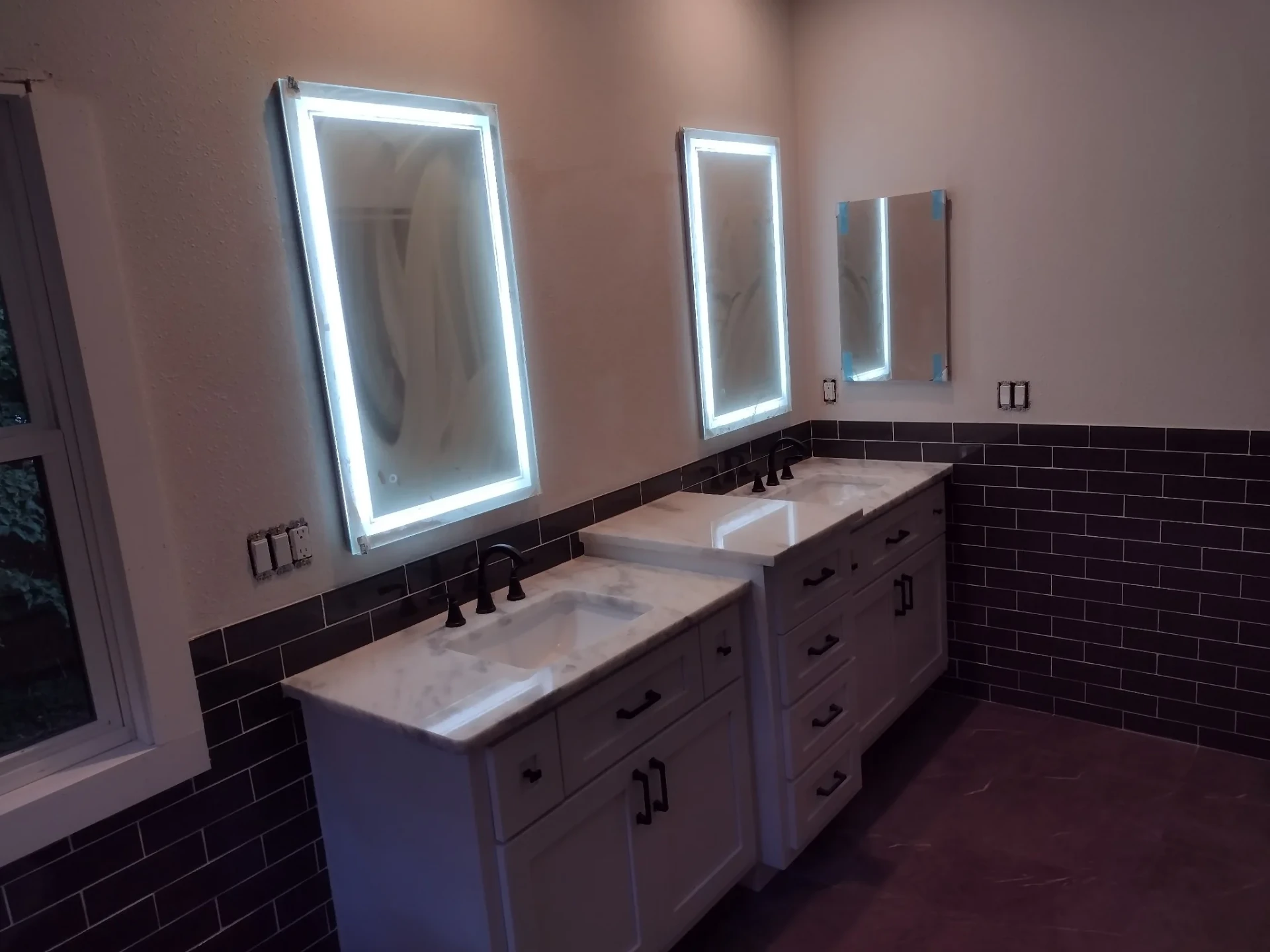 Double white vanities with stone tops, lit mirrors and dark subway tile